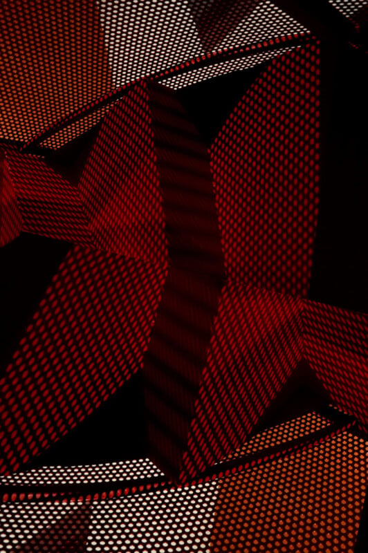 Abstract image featuring red and orange geometric shapes with dot patterns. The composition includes overlapping triangular forms creating a sense of depth and contrast against a dark background.