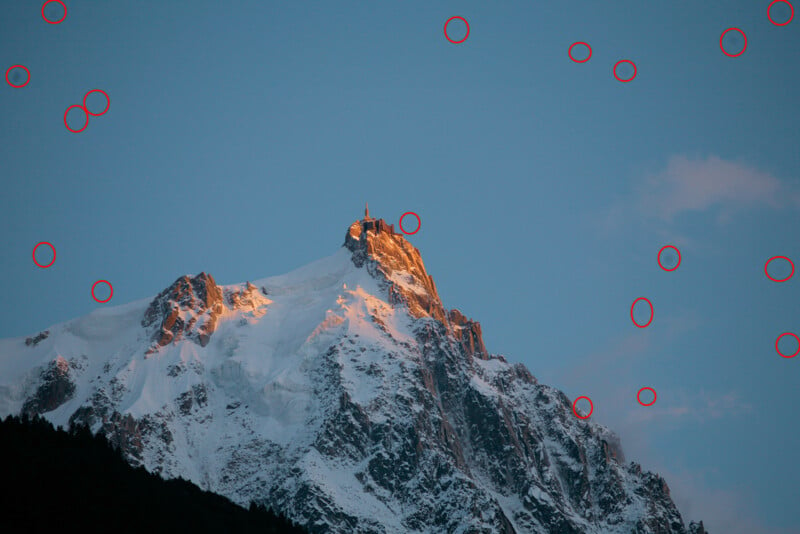 A snow-covered mountain peak is bathed in warm sunlight under a clear blue sky. The peaks are highlighted with touches of golden light. Red circles are drawn around various points in the sky surrounding the mountain.