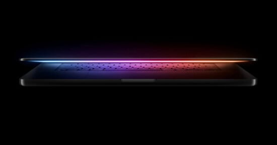 A laptop with a glowing, colorful light emanating from the edges of its slightly open screen, set against a black background.