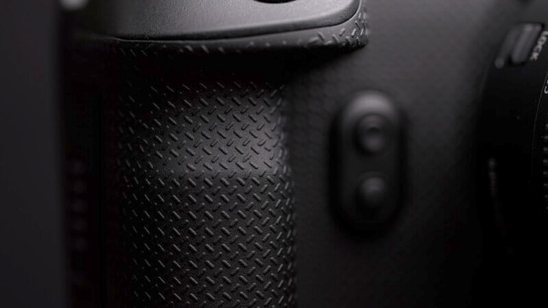 Close-up of a textured black camera grip and button, showing the fine pattern and detail on the camera surface. The image is focused on capturing the tactile design often found on professional camera equipment.