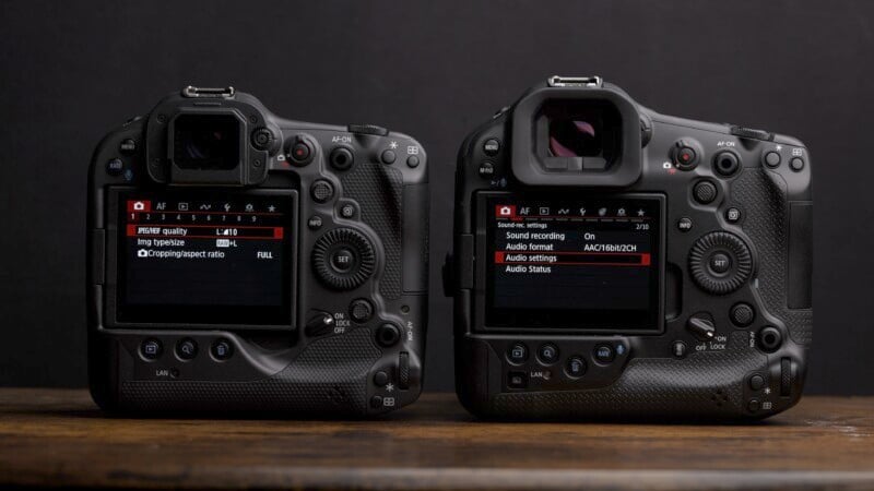 Two professional DSLR cameras are placed side by side on a wooden surface, with screens displaying menu settings for image quality and sound recording. The cameras have a textured grip and multiple buttons, knobs, and dials.