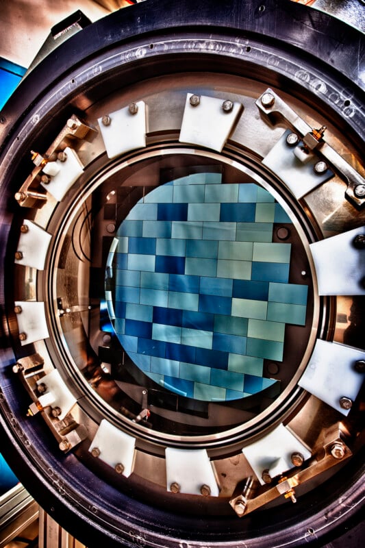 A large, circular scientific instrument features a central blue-tinted mosaic pattern. The outer ring has evenly spaced bolts and a metallic finish, indicating high-tech equipment, possibly used in physics or engineering experiments.