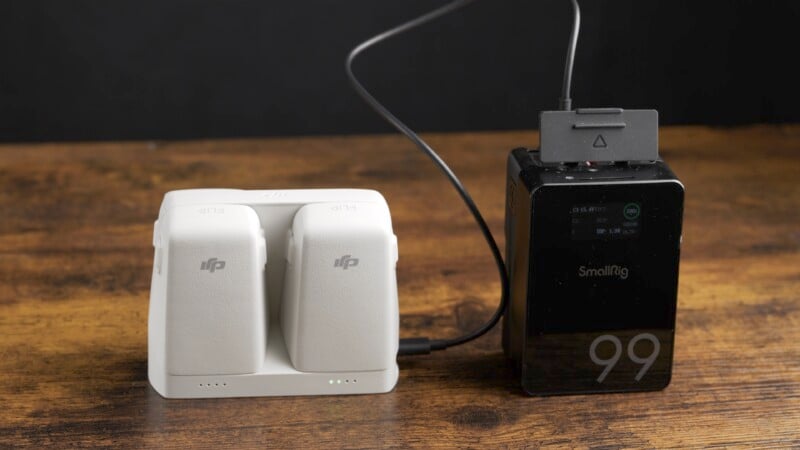 A SmallRig camera battery attached to a charging hub with two DJI batteries on a wooden surface. The SmallRig display shows "99," indicating charge level or capacity.