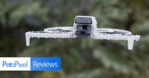 A drone with a camera flying outdoors against a blurred green background. The image has text reading "PetaPixel Reviews" in the bottom left corner.