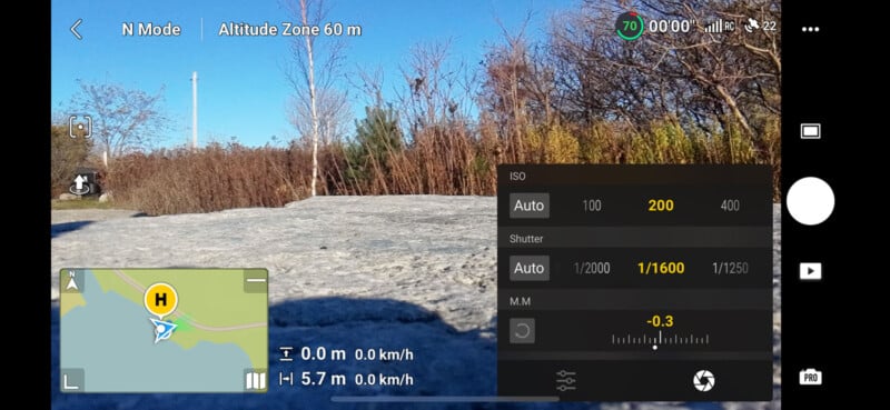 Camera viewfinder displaying a rocky landscape with bare trees under a clear blue sky. Settings include ISO 200, shutter speed 1/1600, and exposure -0.3. GPS map shows location with altitude zone at 60 m.