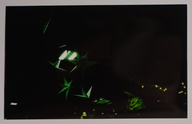 A dark, abstract image featuring green geometric star shapes and beams against a black background. Dim lighting gives the scene an otherworldly ambiance.