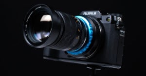 A Fujifilm GFX camera with a large lens is set against a dark background. The camera is positioned on a stand, highlighting its design and the detailed lens features.