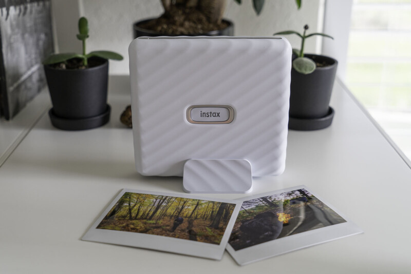 A Fujifiml Instax Link Wide photo printer sits on a shelf with two prints in front of it.