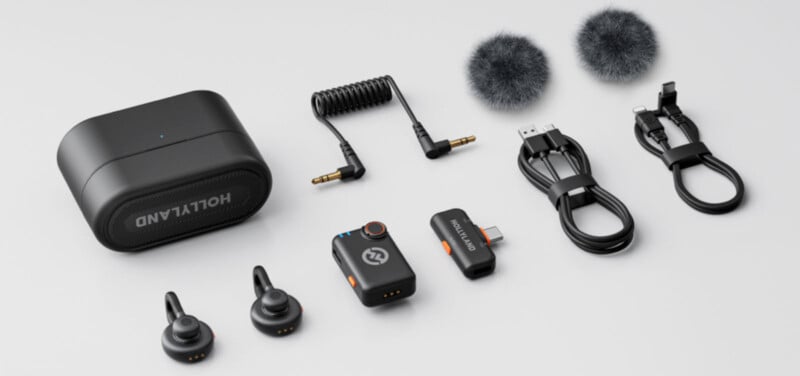 A wireless microphone kit with a charging case, two microphones, a receiver, two furry windshields, audio cables, a USB-C adapter, and charging cables, all arranged neatly on a white background.