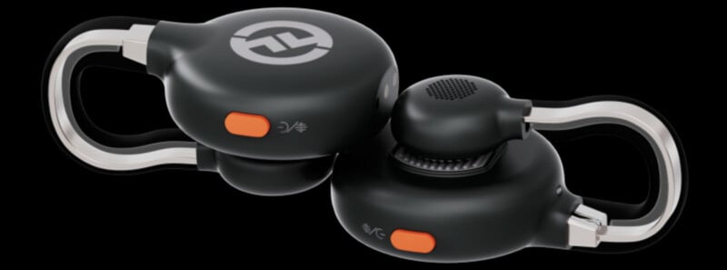 A pair of black wireless earbuds with an orange button and a circular logo on each. The earbuds have a sleek design with transparent loops for secure fit. The background is black, highlighting the earbuds.