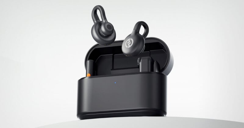 Black wireless earbuds hover above an open charging case against a neutral background. The earbuds have ear hooks for a secure fit. The case features a small LED indicator light.