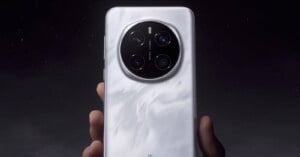 A person holds a smartphone with a sleek, marble-textured white back. The phone has a circular camera module with four lenses and is set against a dark background.