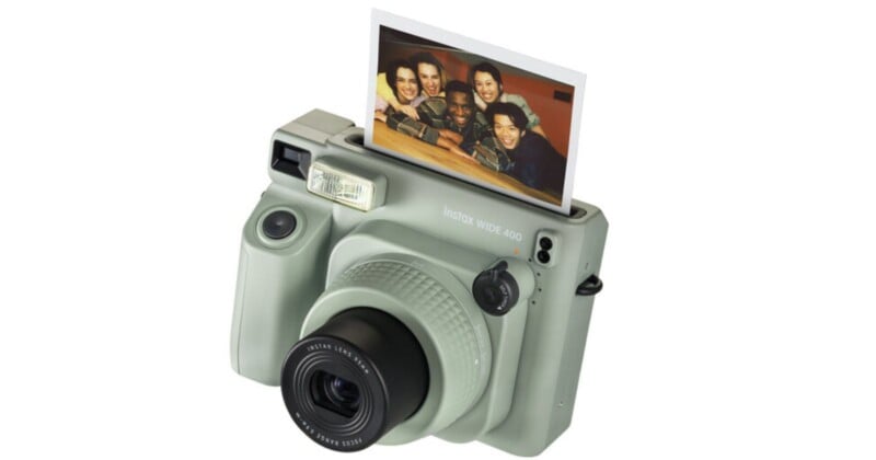 A gray Instax Wide 300 instant camera with a developed photo emerging from the top. The photo shows a group of smiling people gathered closely together. The camera features a large lens and an integrated flash.