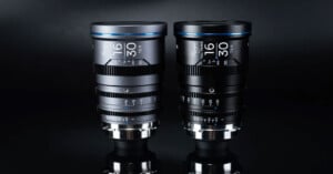 Two professional camera lenses with different focal lengths, placed side by side on a reflective black surface. Both lenses have several adjustment rings and are marked with technical specifications in white.