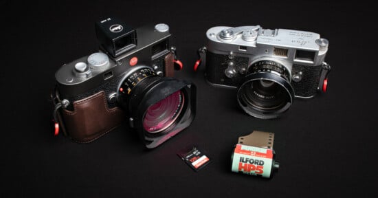 Two vintage cameras with leather straps, a memory card, and a roll of Ilford HP5 film are placed on a black surface. One camera has a red knob and a viewfinder attachment, while the other has a silver finish.