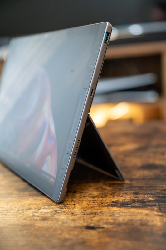 A tablet with a kickstand is positioned at an angle on a wooden surface. The screen displays a colorful abstract pattern. The background is softly blurred, highlighting the device's sleek and modern design.