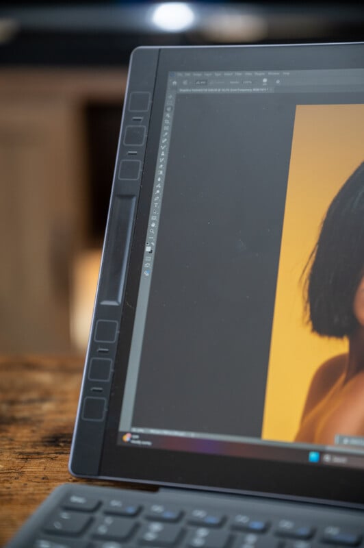 A close-up of a computer screen displaying a graphic design software interface, with a partially visible portrait of a person against a yellow background. The focus is on the screen and tools, with a blurred background.