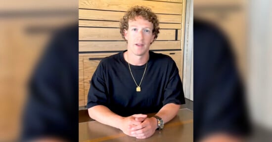 Mark Zuckerberg sits at a table, wearing a black shirt and a gold necklace. The background features wooden panels and a white wall strip.