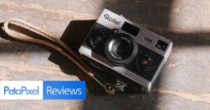 A vintage Rollei 35 AF camera with a wrist strap resting on a wooden surface, partially illuminated by sunlight. A PetaPixel Reviews logo is overlaid in the bottom left corner.