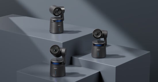 Three black security cameras are displayed on geometric gray platforms. Each camera has a sleek, modern design with blue accent lights. The background is minimal and monochromatic, focusing on the cameras.