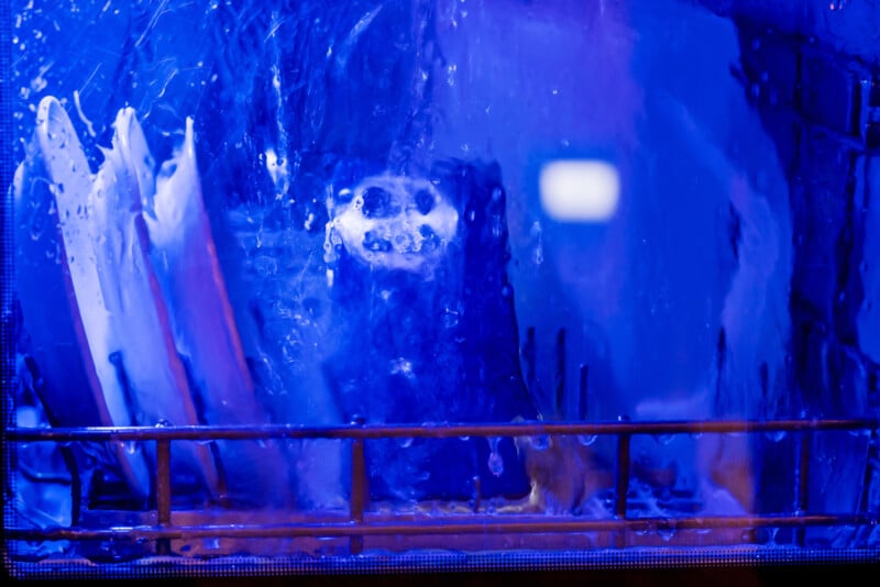 Dishes being washed inside a dishwasher with blue light reflecting off the water and surfaces, creating a vibrant and dynamic appearance. Plates and a cup are visible amidst splashing water.