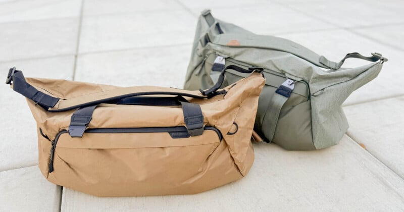 Two duffel bags on a tiled floor: one beige with black straps and the other olive green with matching straps. Both bags have a rugged outdoor appearance and are positioned side by side.