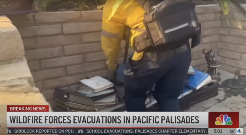 A person in a yellow jacket and backpack is stacking binders and books outside next to a brick wall. The news headline reads, "Wildfire forces evacuations in Pacific Palisades.