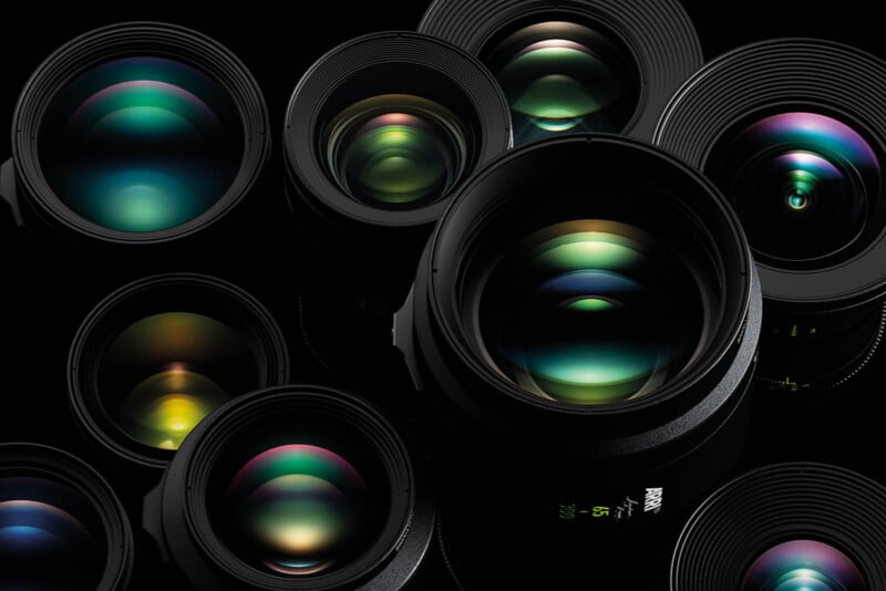 A close-up image of several camera lenses arranged in a cluster against a black background. The lenses are various sizes, and their glass elements reflect vibrant colors, including blues, greens, and purples, creating an artistic and dynamic effect.