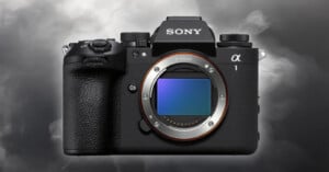 The image shows a Sony Alpha 1 camera, featuring a black body with a prominent grip, numerous control dials, and an exposed sensor in the center. The brand name "Sony" is displayed on the top. The background is a smoky gray.