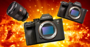 Three Sony cameras on a fiery orange and yellow background. Two cameras have interchangeable lenses, and one lens is shown separately, floating to the left.