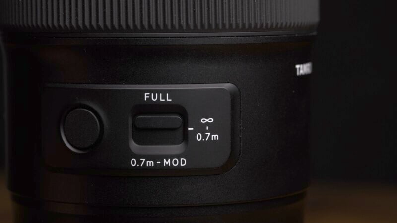 Close-up of a camera lens with a focus mode switch. The switch is set between "Full" and "0.7m," indicating adjustable focus ranges from 0.7 meters to infinity. The lens surface is black with a textured grip area.