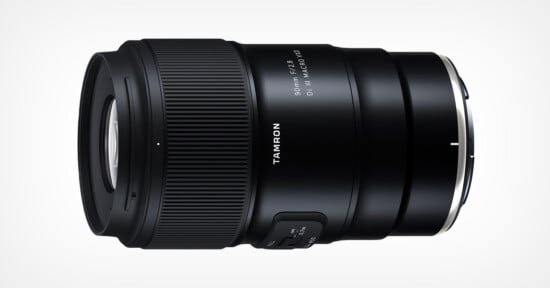 A close-up of a black Tamron 90mm f/2.8 Di III MACRO 1:1 lens. The lens barrel features a focus mode switch and branding details, emphasizing its compact and robust design. The background is plain white, ensuring the lens stands out prominently.