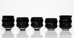 A row of five black camera lenses with silver mounts are displayed against a white background. The lenses vary in size and have detailed markings and numbers on their surfaces.