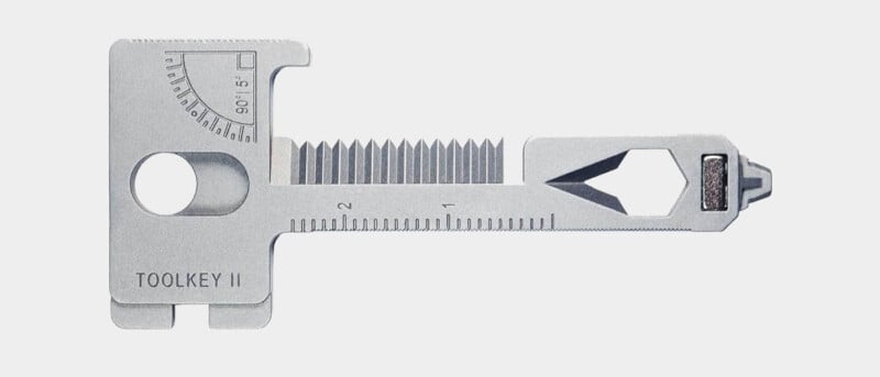 A multi-tool called the Toolkey II is depicted. It includes a ruler, screwdriver, mini wrench, and multiple hex key slots. The tool is compact and flat, made of a metallic material, and designed for portability.