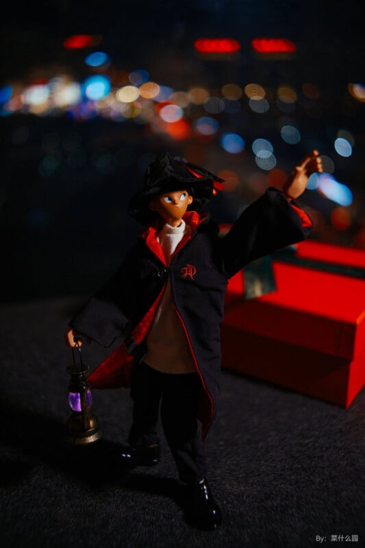 A toy figure dressed in a black robe with red accents and a hat stands with an outstretched arm. It holds a miniature lantern. The background is blurred with bokeh lights, creating a night-time atmosphere.