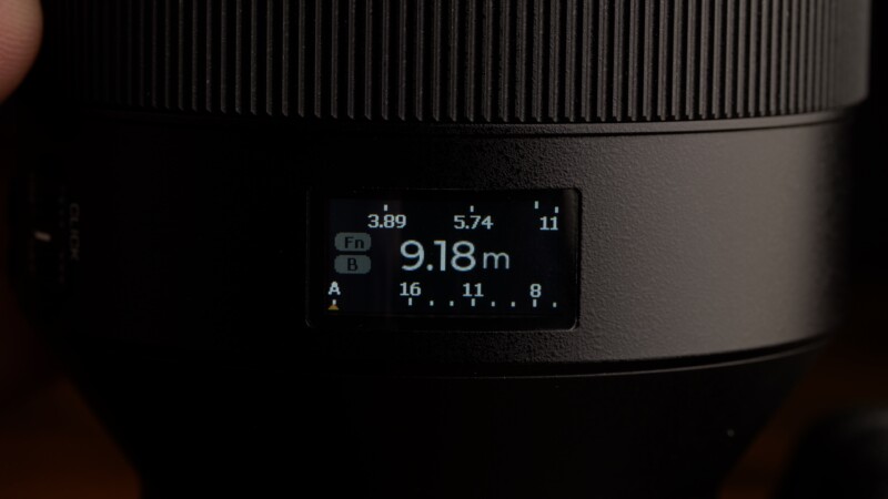 Close-up of a camera lens with a digital display showing a distance of 9.18 meters, aperture settings ranging from 3.89 to 11, and function options labeled "Fn" and buttons "A" and "B.